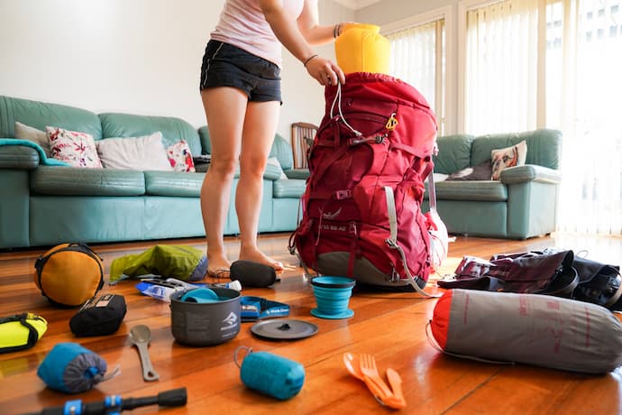 Photo of woman packing backpack for hiking and a lot of hiking essentials on the floor
